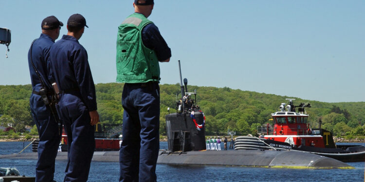 Buque de la Armada de Estados Unidos navegando, escoltado por embarcaciones