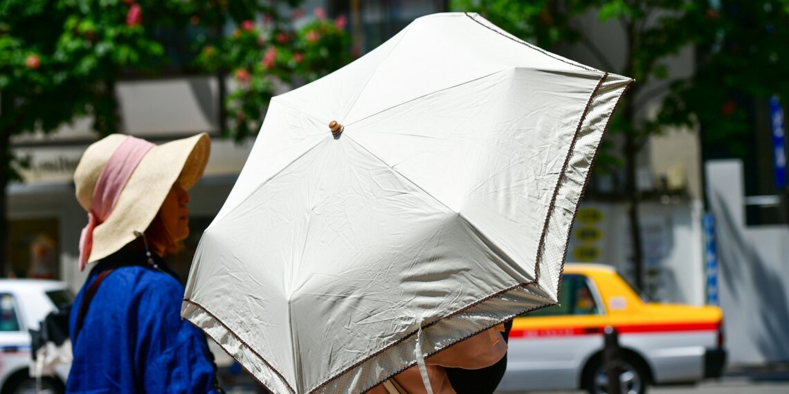 Personas se protegen del intenso sol de verano con sombrilla durante una ola de calor