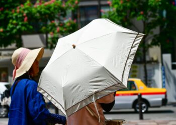 Personas se protegen del intenso sol de verano con sombrilla durante una ola de calor