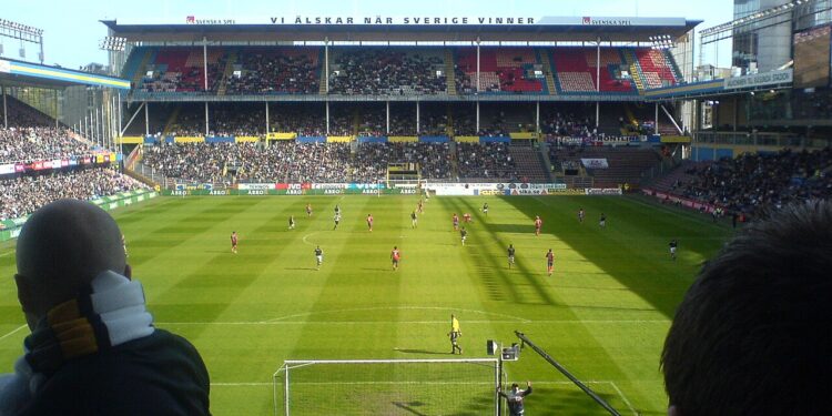 Jugadores disputan un partido de fútbol en un estadio lleno de aficionados