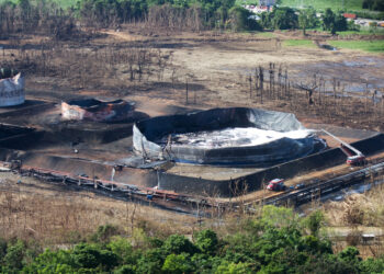 Equipo de bomberos junto a tanques de petróleo incendiados en una refinería
