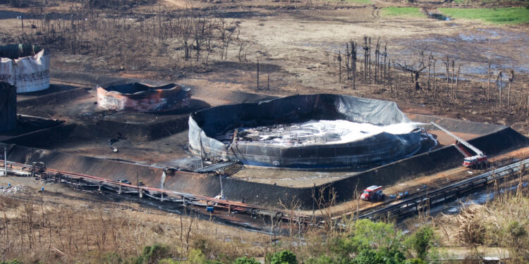 Equipo de bomberos junto a tanques de petróleo incendiados en una refinería