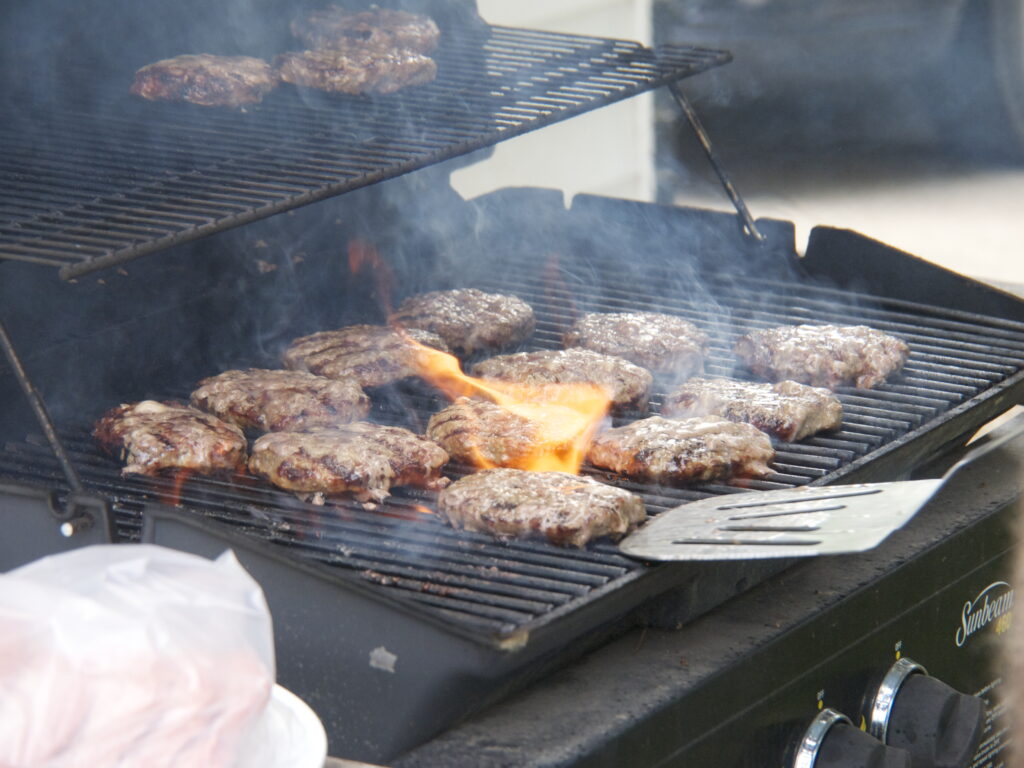 Hamburguesas cocinándose en una parrilla al aire libre durante una reunión