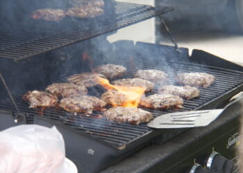 Hamburguesas cocinándose en una parrilla al aire libre durante una reunión