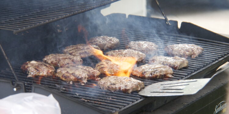 Hamburguesas cocinándose en una parrilla al aire libre durante una reunión