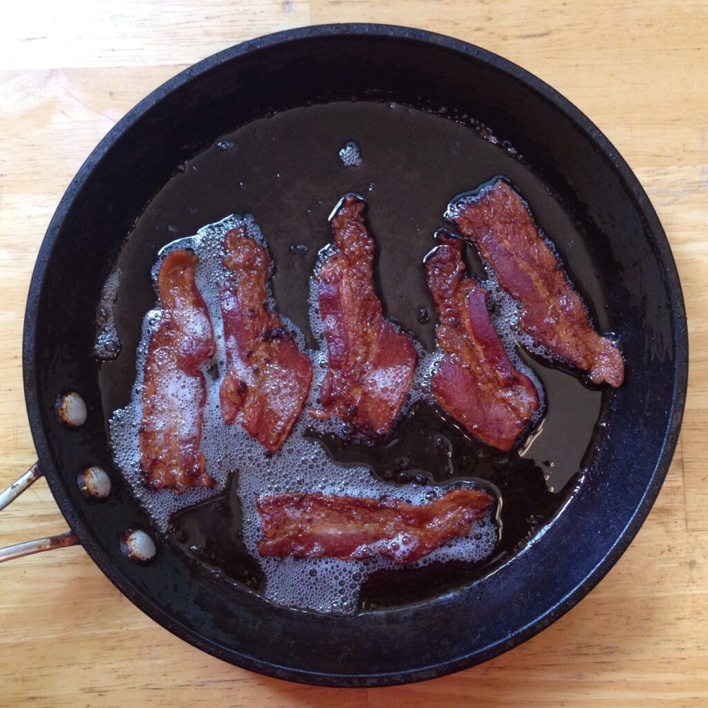Tiras de tocino cocinándose en una sartén