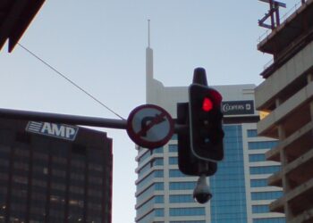 Poste con semáforos y una cámara de vigilancia sobre una calle