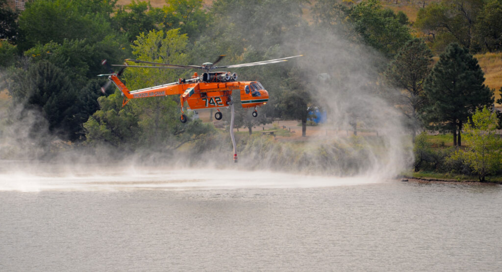 Helicóptero de bomberos con cubo de agua sobrevolando durante labores contra un incendio forestal