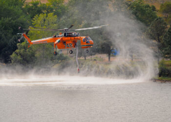 Helicóptero de bomberos con cubo de agua sobrevolando durante labores contra un incendio forestal