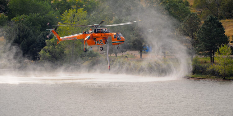 Helicóptero de bomberos con cubo de agua sobrevolando durante labores contra un incendio forestal
